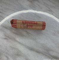 Roll of 50 1964 US pennies wrapped in a paper coin roll, labeled with '60¢ 50 Pennies' and handwritten '1964'.