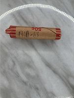 Photo of a paper-wrapped roll of pennies labeled '1960-63' on a marble-like surface.