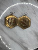 Photo of front side of pair of large hexagonal-shaped brass-tone metal earrings with basket-weave circular inlay pattern in center on a marble surface.