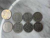 Obverse side view of eight 100 yen coins showing denomination and year