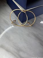 Pair of gold hoop earrings with diamante bird embellishments resting on a marble surface near a blue box.