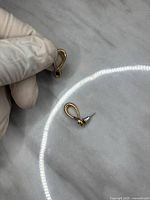 Two gold-tone looped drop earrings with teardrop design, held by gloved hand showing detailed condition and scratches.