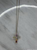 Full view of gold-tone chain necklace with a cross pendant featuring multiple colored gemstones and diamond accents on a marble surface.