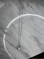 Full view of the necklace with heart-shaped pink opal pendant on a marble surface, showing chain and pendant.