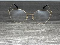 Front view showing gold metal frame eyeglasses with angular lenses and Valentino branding on one lens, on wooden surface.
