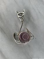 Front of vintage silver cat-shaped pendant with purple polished stone as the body on a light surface.