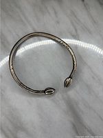 Two images showing a vintage West Indies sterling silver open cuff bangle bracelet with petal-shaped ends and etched detailing on the band, displayed on a marble surface with natural lighting.