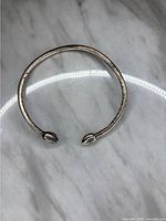 Full view of one vintage sterling silver open cuff bangle bracelet showing its round band and decorative end tips shaped like leaves or petals.