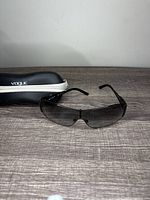 Front view of Vogue VO 3640SB sunglasses with black gradient lenses on grey wood surface, hard case in background.