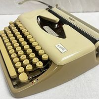 Front and side angled view of beige Triumph Tippa 1 typewriter showing keyboard, logo plate, and platen lever
