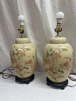 Full view of the pair of beige and hand painted floral ginger jar style table lamps with black bases and electric fittings without shades.
