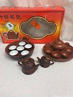 Two sets of miniature Chinese clay tea pots with matching cup trays, displayed with original box in background