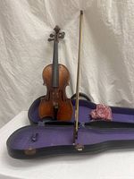 Overview of violin standing in open hard case with bow resting inside, red cloth accessory visible