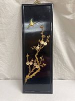 Full view of tall rectangular black lacquered wooden panel with carved flowering branches and bird design.