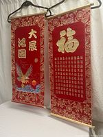 Two red Chinese Feng Shui scroll wall hangings side by side, showing gold calligraphy and decorative borders
