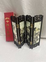 Miniature Japanese lacquered four-panel table screen standing partially folded on surface, showing painted landscape and fish motif panels.