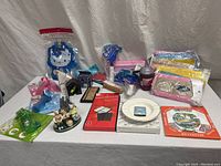 Wide shot showing the full lot of vintage souvenir and gift items spread on a plain background. Items include Hello Kitty themed items, figurines, decorative plate, card game boxes, and small collectibles.
