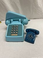 Front view of turquoise Western Electric 1500 touch-tone desk phone with mini blue rotary phone sales sample beside it.