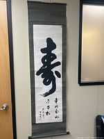 Full view of vintage calligraphy scroll hanging on wall, showing main large character and fabric border.