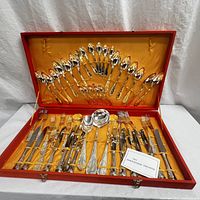 Overview of entire silver plated cutlery set for 12 in the open red case with satin lining, showing all pieces arranged.