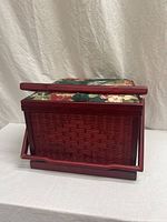 Side view of vintage woven wicker sewing basket with floral cushioned lid and foldable wooden handles resting on white surface with neutral background