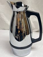 Close up of the chrome coffee server from the side showing reflective surface and geometric handle design.