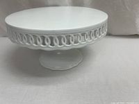 Front angled view of white porcelain cake/display pedestal highlighting smooth top surface and loop border design.
