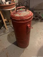 Front view of the tall red metal milk can showing dented lid, carry handle, and overall wear.