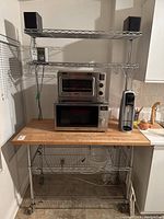 Full view of bakers rack showing wood worktop with microwave, toaster oven, and soda maker on top and wire shelves below.