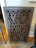 Close-up photo of one carved wood panel showing the intricate leaf and scroll pattern within a rectangular wooden frame.