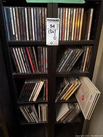 Full view of shelving unit with eight cubbies filled with CD jewel cases mostly in rock and pop genres. Shows a variety of CD titles stacked vertically.