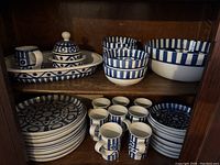 Top shelf: rectangular baking dish/tray, creamer, sugar bowl with lid, three smaller bowls and large serving bowl. Bottom shelf: stacked dinner plates, salad plates and mugs.