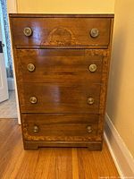 Front view of dresser showing four drawers, burl veneer inlay, carved trim and round brass knobs