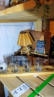 Wood lamp with wood slat-style shade beside four clear glasses on wooden serving board and small painted slate art on easel