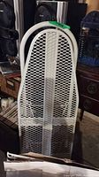 White metal mesh ironing board leaning against furniture