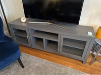 Front view of gray media cabinet with two glass doors and open center shelf, showing TV and decorative items on top.