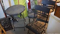 Photo showing entire patio set: round folding metal table, two folding slatted metal chairs, and one smaller decorative metal chair with heart-shaped back.