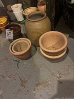 Overview of clay and ceramic plant pots on floor including large ribbed pot, stacked and individual smaller pots