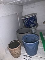 Overview of five ceramic plant pots showing variety of colors and shapes including blue patterned, gray, beige, and light blue pots.