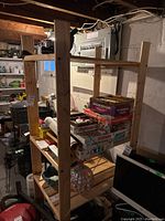 Wood utility shelving unit with items stored on shelves in a basement. Visible electrical panel and wooden ceiling beams in background.