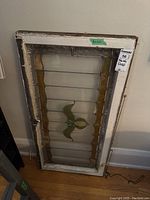 Full view of antique wooden framed stained glass panel leaning against a wall with visible floral design and ribbed glass sections.