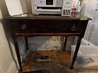 Front view of vintage wooden side table showing drawer and turned legs with scuffs and marks