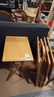 Four wooden folding TV tables, one set up with stand, others stacked folded, showing wood grain and scratches.