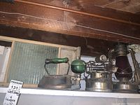 Photo showing vintage washboard, flat iron with green handle, Coleman single burner stove, and lantern on shelf.