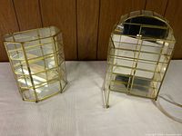 Two miniature brass and glass display cases side by side on fabric surface.