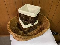 View of two small dark brown wicker baskets with white fabric liners placed inside a large light brown oval wicker pet bed basket.