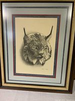 Framed print of a lynx by Albert J Casson with visible signature, matted and framed in black and gold.