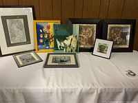 Collection of eight cat-themed framed decorative art pieces on a cloth-covered table showing variety and style.