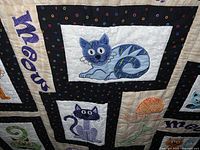 Close-up photo of the quilt's embroidered cat designs and 'meow' text.