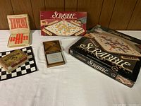 Photo showing two Scrabble games in their boxes with letter tiles, a small checker board with checkers, Tangram set, and Hi-Q game with pegs.